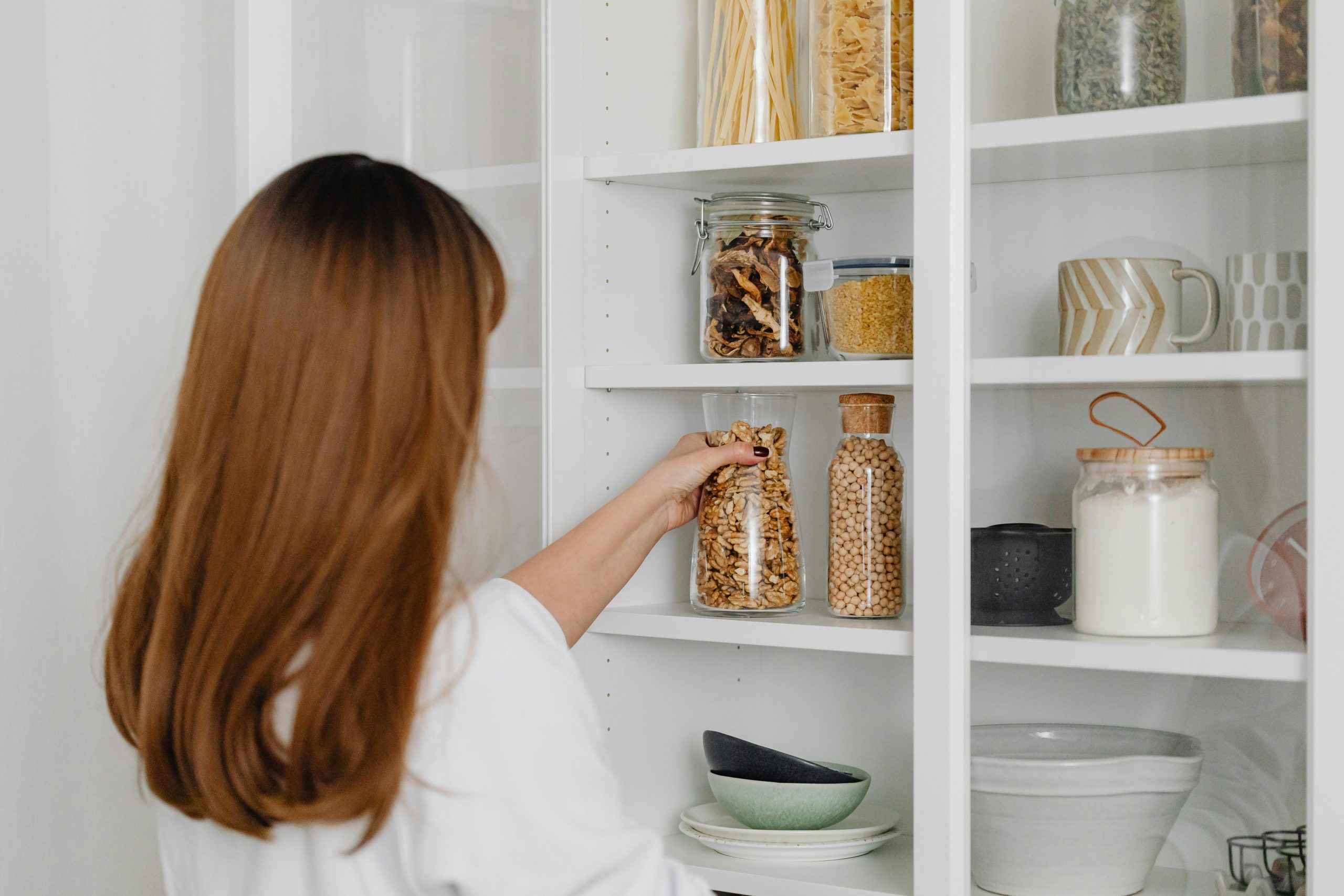 a woman reaching for a glass jar of cereal in an organised kitchen cupboards